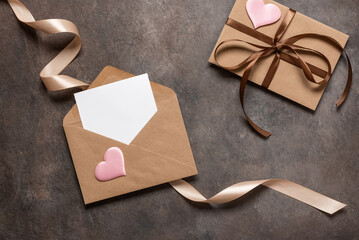 Open brown envelope flat lay with blank card decorated with silk ribbon and silk hearts on dark vintage background. Valentine's Day card. Top view.
