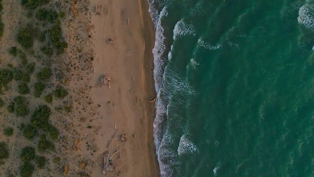 Tuscany sandy beach waves in slow motion by sunset. Maremma, Italy, seaside aerial.