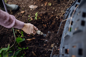 Girl removing compost from a composter in the garden. Concept of composting and sustainable organic...