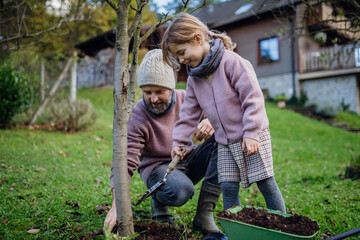 Girl and father planting tree in garden in the spring, using compost. Concept of sustainable...