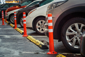 Car parked close to flexible plastic warning post. Cars parked in row close to plastic parking barrier, orange anti parking bollard on parking lot at downtown. Public parking place in downtown. - obrazy, fototapety, plakaty