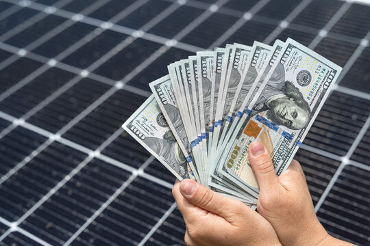 Business man hold us dollar bills as saving const after instalation solar photovoltaic panel