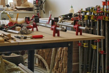 Craft carpentry workshop with variety of wooden pieces and planks, hand tools and wooden work bench in the foreground. Joinery with workbench and lots of wood. Carpenters table with furniture details