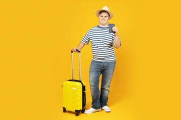 Smiling young man with down syndrome in glasses with suitcase and hat