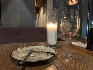 End of dinner. Leftover dinner on a wooden table. An empty plate and a glass of wine and a candle