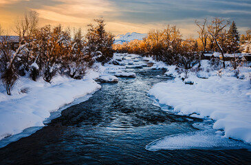 Beautiful view of partially frozen stream in Colorado at sunset; mountain and sunset sky in background - obrazy, fototapety, plakaty