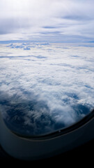 Scenic nature view from an airplane window during flight above white clouds against a blue sky...