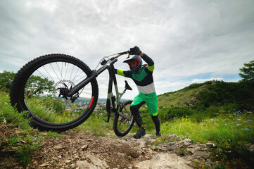 Fototapeta na wymiar A man pushes a mountain bike up a hill. Adventure travel by bike. Guy athlete in defense lifts his equipment