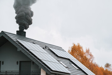 Dark smoke comes out of the chimney of a modern house during the late autumn and winter. Heating...