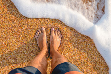 male feet barefoot on the waves of sea foam on a sandy golden beach on a summer day. top view of...