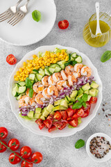 Shrimp salad with vegetables and olive oil mustard dressing. Fresh seafood salad on a white plate on a gray concrete background. Healthy food. Copy space.