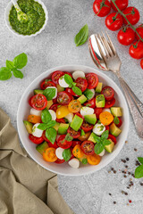 Caprese salad with cherry tomatoes, mini mozzarella balls, avocado, pesto sauce and fresh basil. Healthy vegetarian meal.