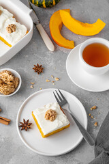 Spiced pumpkin cake with walnut and cream cheese frosting sliced into squares on a gray concrete background. Autumn dessert.