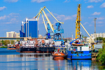 Cargo ships stand in the port of Astrakhan on the Volga River, Astrakhan cargo port. Port cranes. - obrazy, fototapety, plakaty