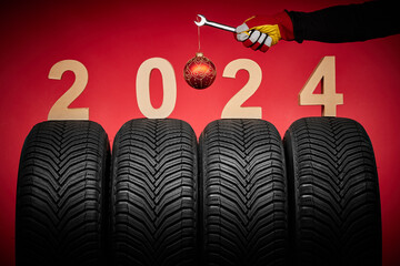 Winter car tires, big wheels service and hand of mechanic man with wrench and christmas ball on red...