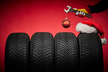 Winter car tires service and hands of mechanic, wrench screwdriver, christmas ball happy new year red background.