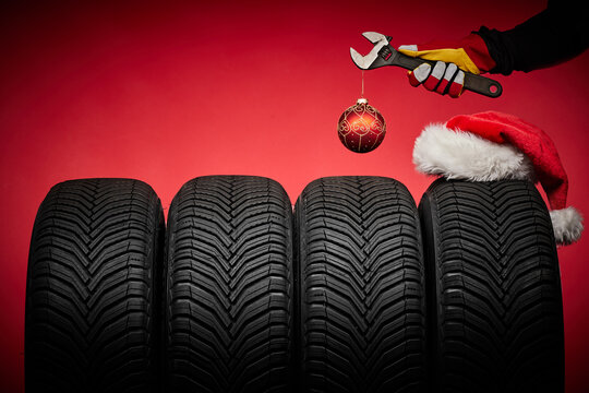 Winter car tires service and hands of mechanic, wrench screwdriver, christmas ball happy new year red background. - Powered by Adobe