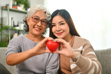 Obraz na płótnie Canvas Beautiful middle age mother and daughter holding red heart. Health care, insurance and world heart day concept