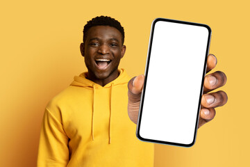 Excited African man in studio holding large smartphone blank screen