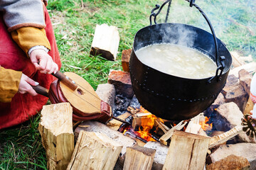 Cooking in medieval style. A woman in national costume starts a fire with an old blower. The cook...