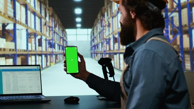 Delivery industrial advisor shows greenscreen display in warehouse storage room, working on cargo logistics for new order shipment. Depot supervisor holds isolated chromakey device.