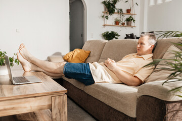 A man is relaxing after a working day, sitting on the couch and watching a TV show or movie through...