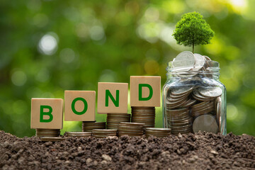Green bonds concept. Words BOND on a wood block place on coin stack and glass coin jar with tree on...