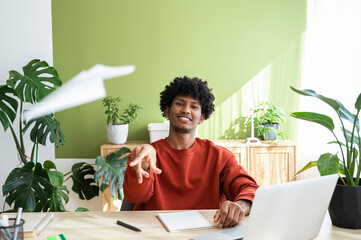 Smiling young freelancer playing with paper airplane sitting at home office