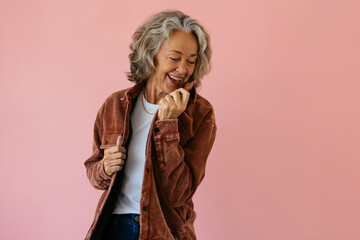 Smiling senior woman wearing brown jacket and standing against pink background