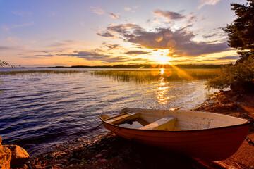 Sweden, Gavleborg County, Hedesunda, Empty rowboat lying onLakeshoreat sunset