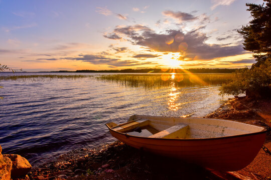 Sweden, Gavleborg County, Hedesunda, Empty rowboat lying onLakeshoreat sunset