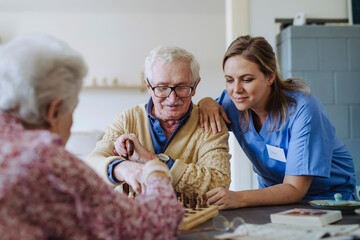 Smiling healthcare worker playing chess with senior couple at home