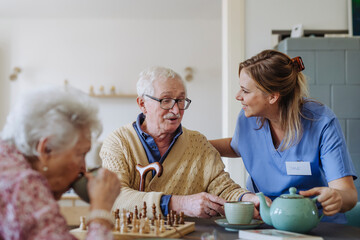 Happy healthcare worker serving tea to senior couple at table