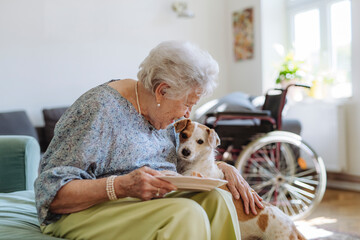 Happy senior woman holding plate of food and stroking dog at home