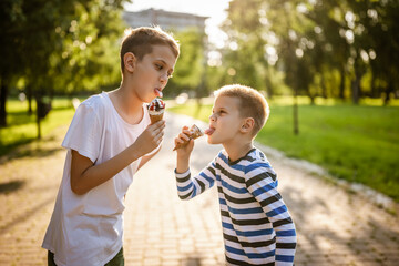 Two brothers are eating ice cream in park in summer. They are having fun and mocking at each other.