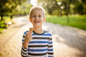 Portrait of happy boy who is standing in park and eating ice cream.