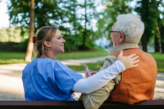 Happy healthcare worker supporting and consoling senior man on bench at park