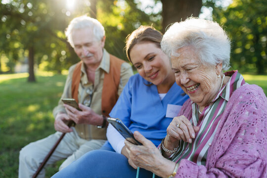 Happy healthcare worker with senior man and woman using smart phone in park
