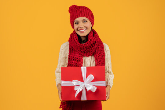 woman in red knitwear holding Christmas gift box, yellow backdrop