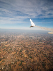 View from an airplane window of a populated area and left wing, warm sunny day. Travel and tourism view. Flying to holiday destination point. Scene through illuminator. High viewpoint.