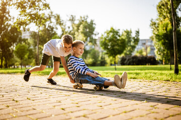Two boys are having fun with skateboard in park. Playful children in park, happy childhood.