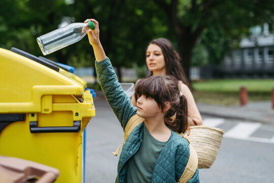 Mother and schoolgirl daughter separate waste into recycling bins in the city