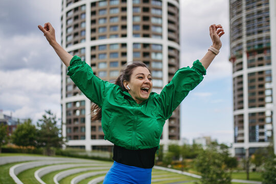 Beautiful woman exercises in a city park raising arms happily