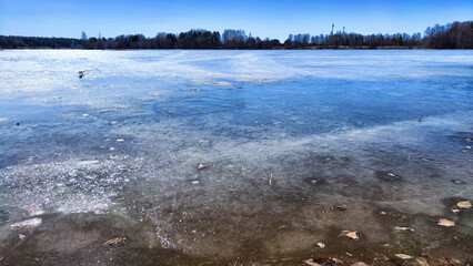 Landscape with a lake covered with ice before the start of melting and ice drift on a spring day with the sun. Blue ice and water under sunlight in early spring or autumn