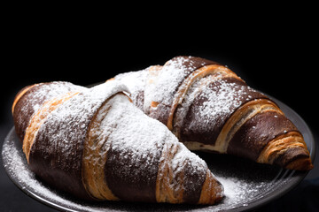 Chocolate croissants with powdered sugar on a black background, close-up. Homemade baked goods