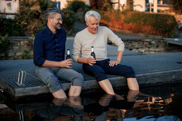 Happy senior friends sitting on pier with beer bottles
