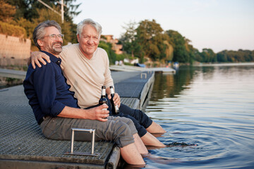Happy senior man enjoying beer with friend on jetty