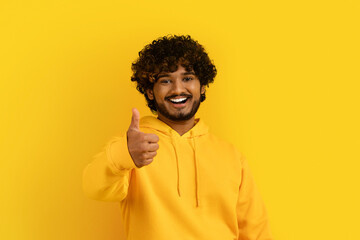 Fototapeta na wymiar Happy young indian guy showing thumb up on yellow background