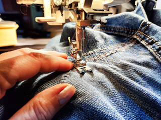 Sewing machine and blue jeans fabric. A woman's hand and fingers next to a sewing machine needle...