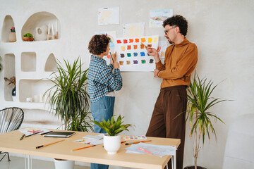 Graphic designer discussing with colleague over color swatch on wall at office